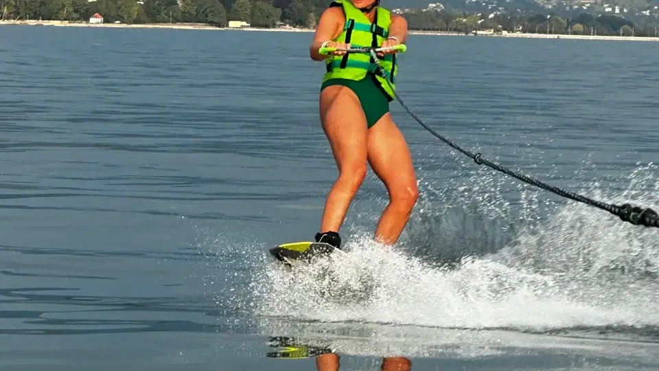 Wakeboardende Person mit grüner Weste und Helm auf dem See