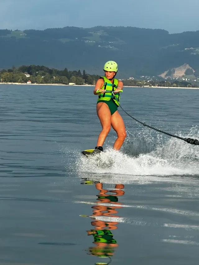 Wakeboardende Person mit grüner Weste und Helm auf dem See
