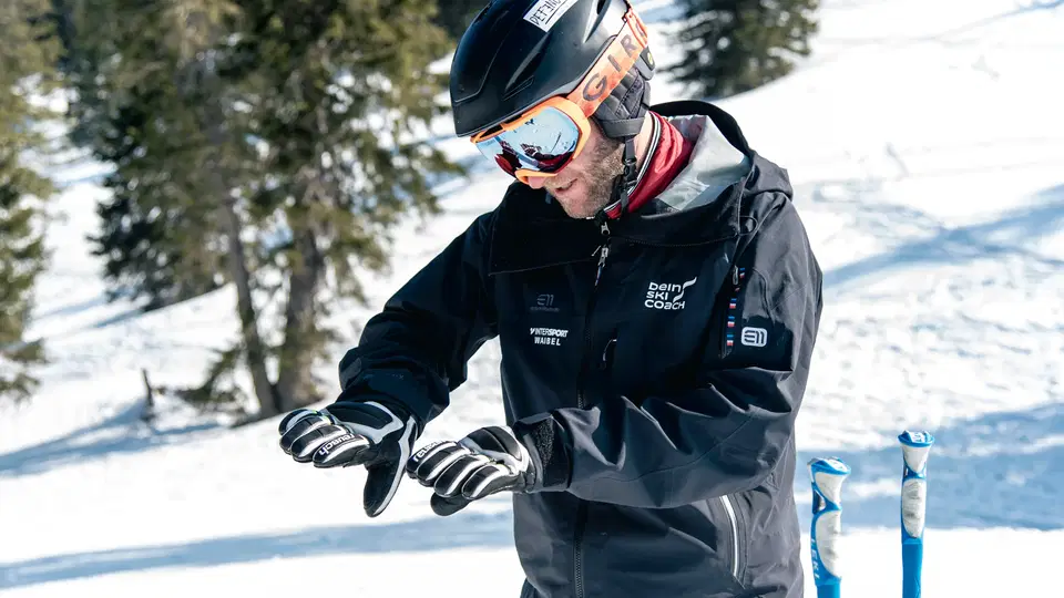 Ski-Coach mit Helm und Skibrille überprüft Handschuhe im Schnee