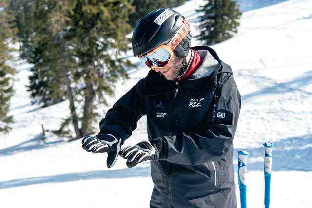 Ski-Coach mit Helm und Skibrille überprüft Handschuhe im Schnee
