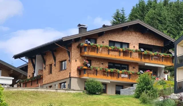 Haus Alpenglück am Hang mit Holzbalkonen und Blumenkästen