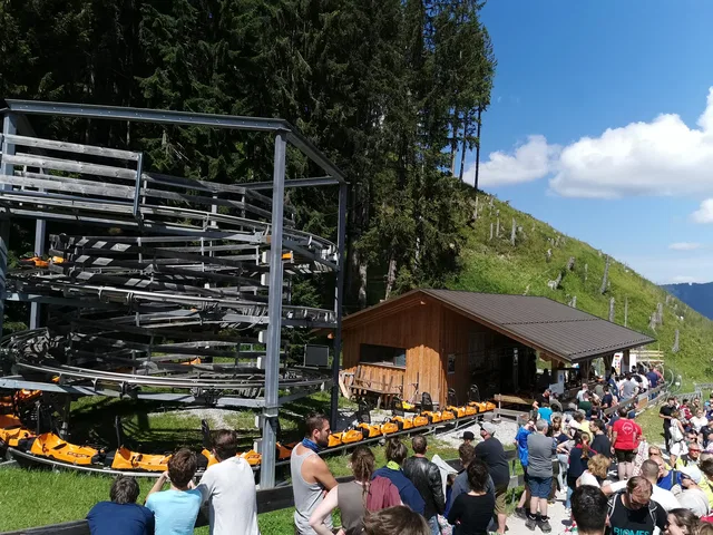 Größere Menschenmenge an einer Berghütte mit gestapelten Sessellift-Gestellen im Vordergrund