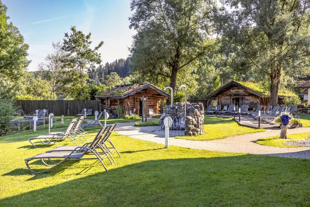 Sonnenliegen auf Gras vor rustikalen Holzhütten im Wellnesspark