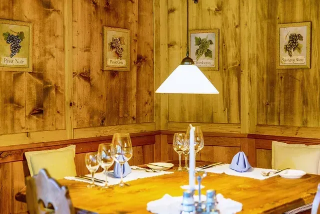 Gedeckter Holztisch in rustikalem Restaurant mit Holzwänden und Weinbildern an der Wand.