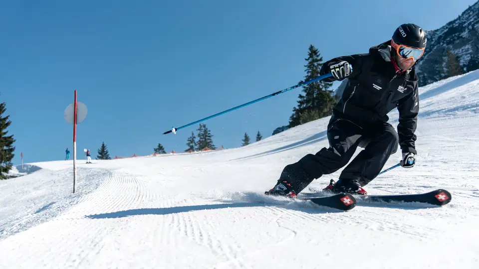 Skifahrer in schwarzer Kleidung fährt kurvenreich auf der Piste unter blauem Himmel.