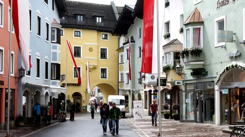 Straße in farbenfroher Altstadt mit Bogendurchgang, bunten Gebäuden und roten Flaggen.