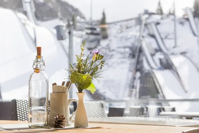 Tisch mit Blumenvase in der Erdinger Sportalp vor den verschneiten Skisprungschanzen