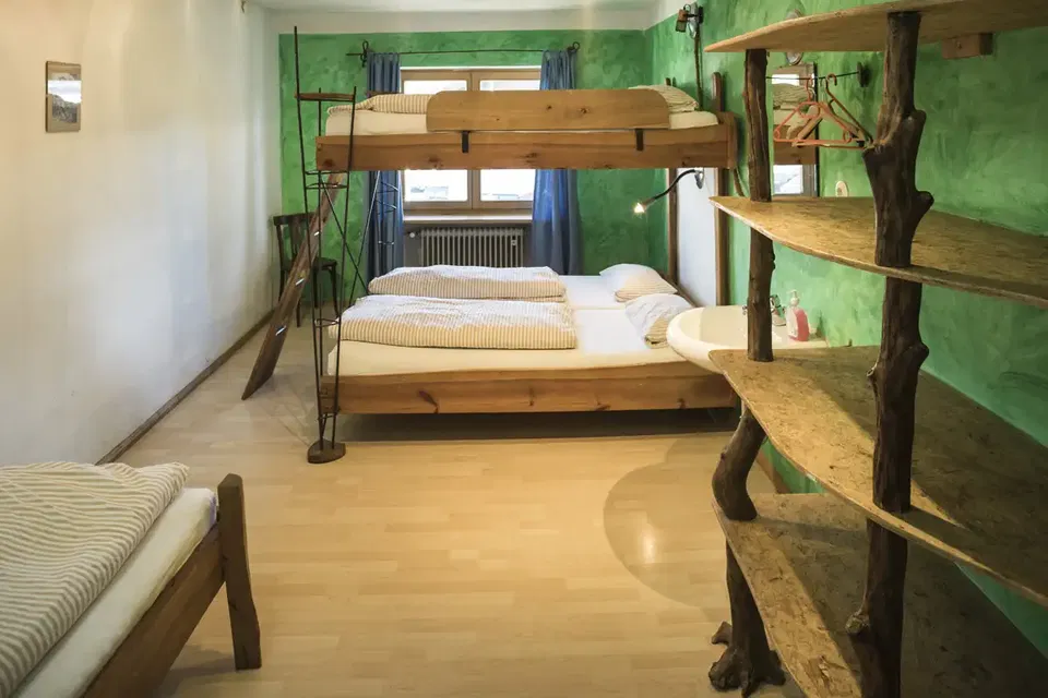 Zimmer Jungle mit Holzstockbett, zusätzlichem Einzelbett und Regalen an grüner Wand