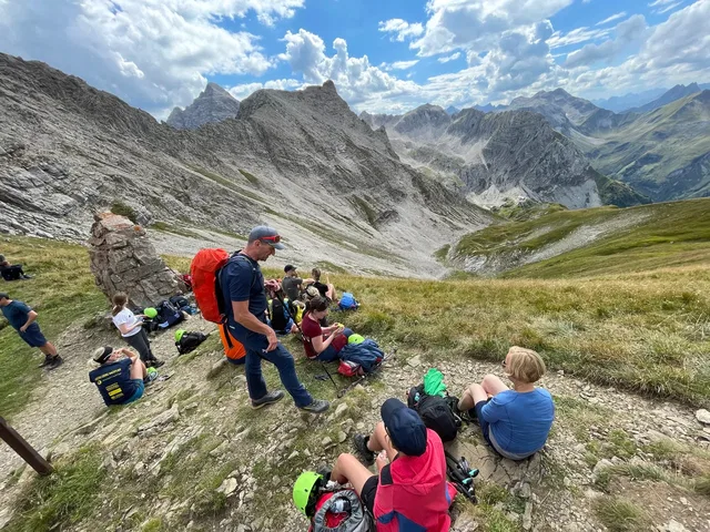 Wandergruppe rastet vor einer zerklüfteten Berglandschaft.
