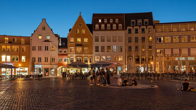 Beleuchtete Häuser und Straßencafés am Augsburger Rathausplatz zur blauen Stunde