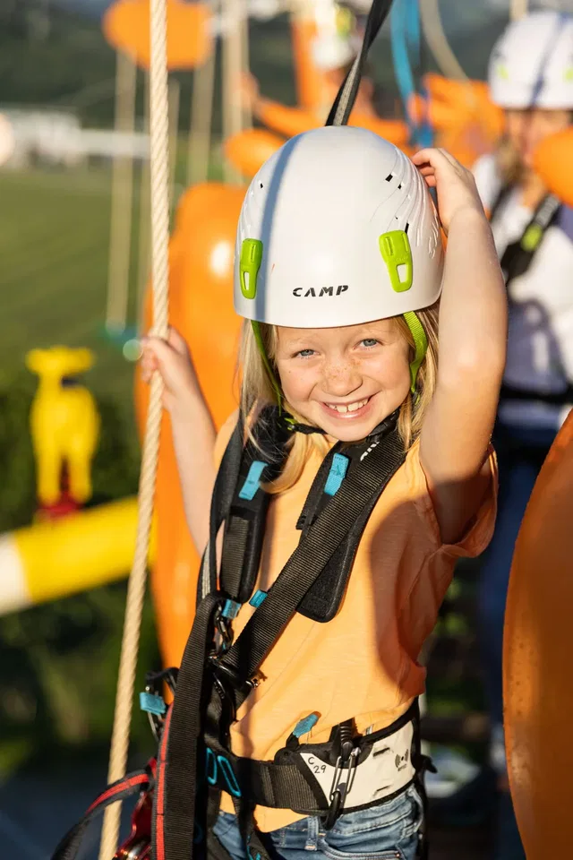 Klettergast mit Helm und Gurt vor einem orangefarbenen Element