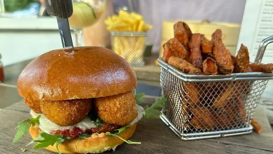 Burger mit panierten Füllungen und Beilagen im Metallkorb auf einem Holztisch