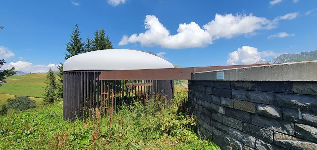 Skyspace-Lech von außen mit Kuppel, Steinmauer und Bergwiesen