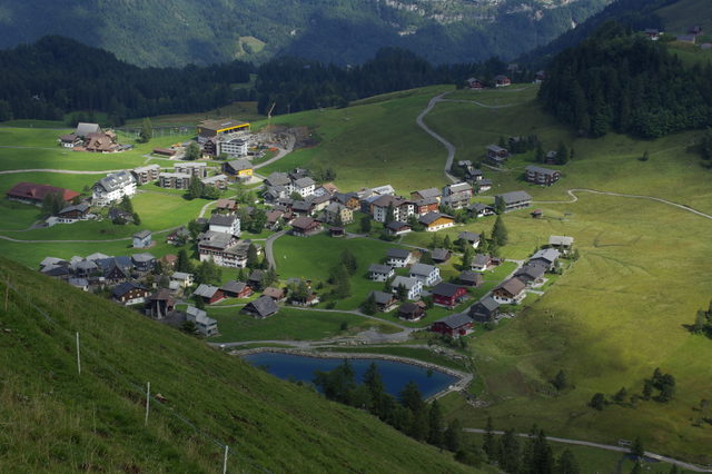 Bergdorf Stoos mit dem Stoos-Seeli im Vordergrund und grünen Hängen