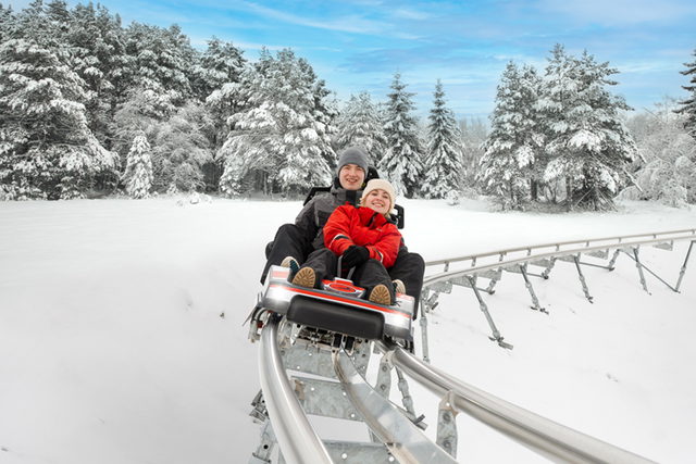 Zwei Fahrgäste im AlpspitzCOASTER vor verschneiten Bäumen.