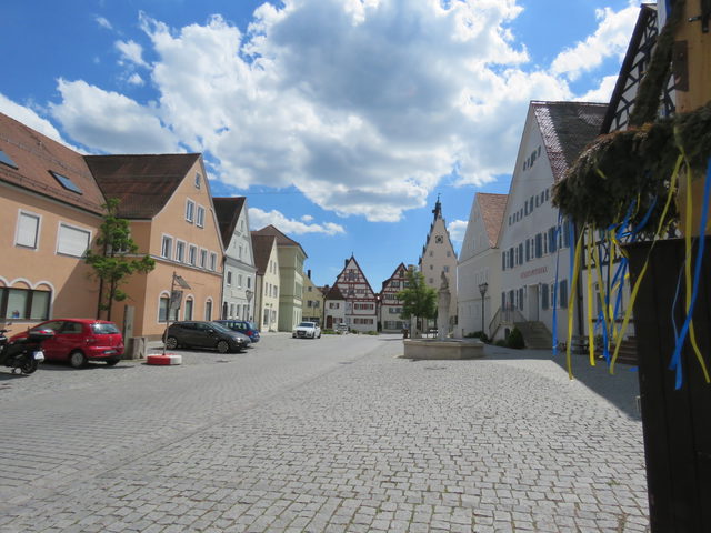 Gepflasterter Marktplatz von Monheim in Bayern mit Brunnen, historischen Häusern und Maibaumdetail rechts