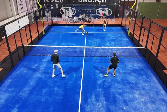 Vier Spieler beim Doppel auf einem blauen Padelcourt in der Halle