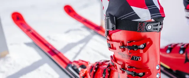 Roter Skischuh mit Schnallen, Skier im Schnee im Hintergrund