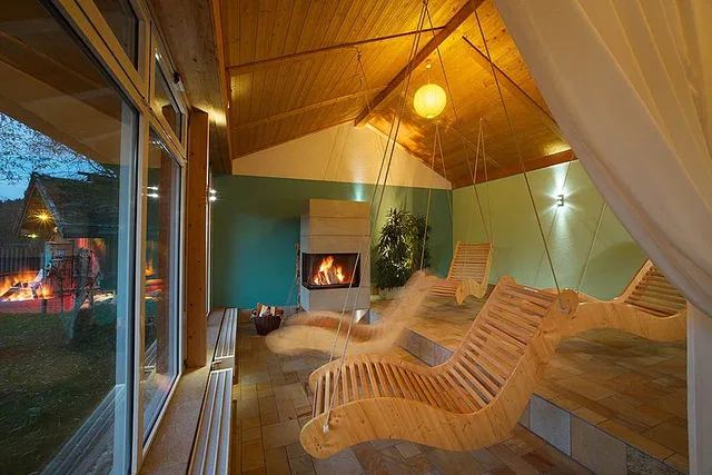 Hängende Holz-Loungesessel im Ruheraum vor Kamin und Glasfenstern.