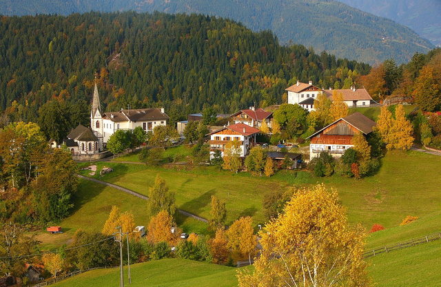 Hafling mit Kirche und Häusern zwischen herbstlichen Wiesen und Bergwald
