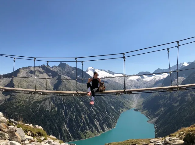 Person auf Hängebrücke über Bergsee mit Bergen im Hintergrund