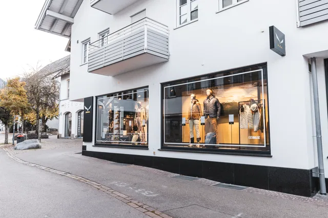 Schaufenster eines Modegeschäfts mit Winterjacken auf Modellen vor einem weißen Gebäude.