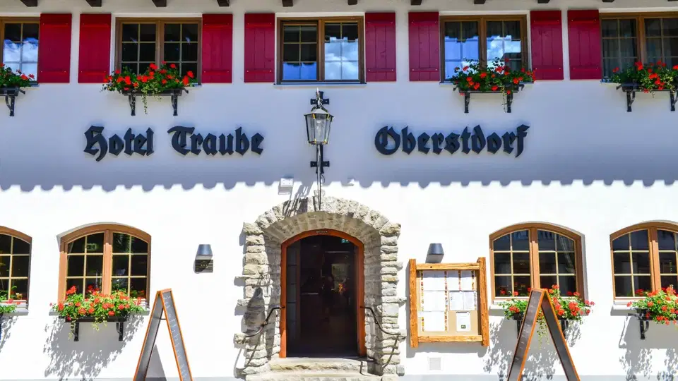 Fassade des Hotel Traube in Oberstdorf mit roten Fensterläden und Blumen