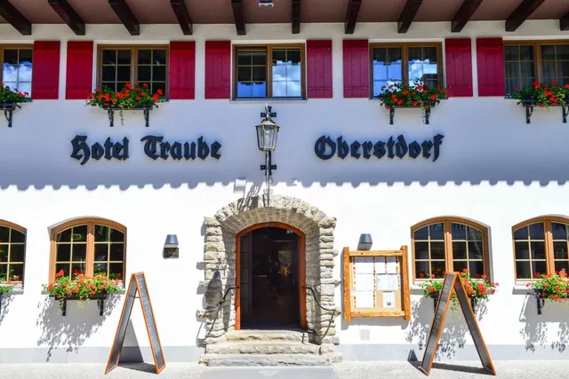 Fassade des Hotel Traube in Oberstdorf mit roten Fensterläden und Blumen