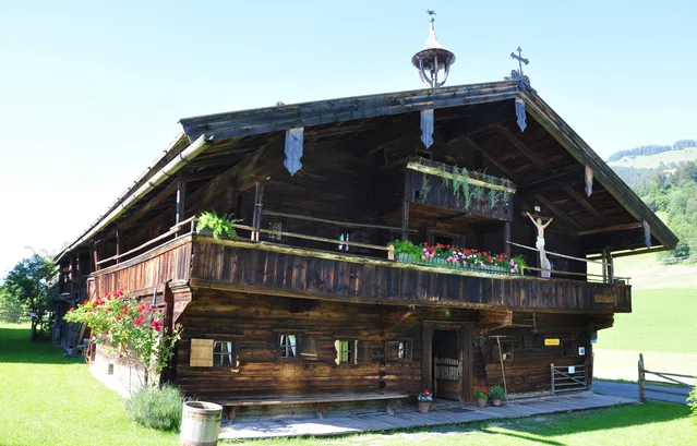 Traditionelles Holzchalet mit Blumen auf der Veranda in grüner Landschaft.