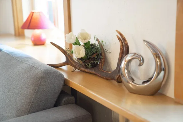 Dekoratives Hirschgeweih mit weißen Rosen auf einer Holzablage neben einer silbernen Skulptur.