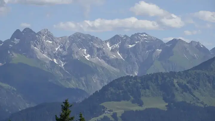 Weite Berglandschaft mit schneebedeckten Gipfeln und grünen Tälern.