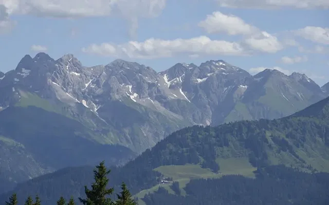 Weite Berglandschaft mit schneebedeckten Gipfeln und grünen Tälern.