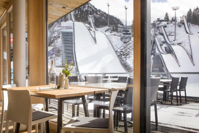 Café-Tisch im Innenraum, Blick durch Glasfenster auf Skisprungschanze im Winter.