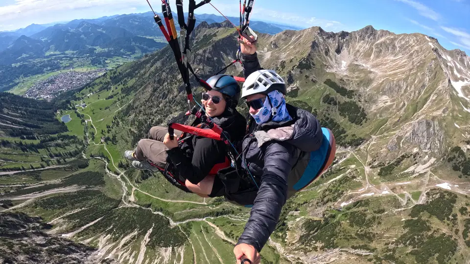Tandemflug über Bergpfaden mit dem Tal und Ort im Hintergrund.