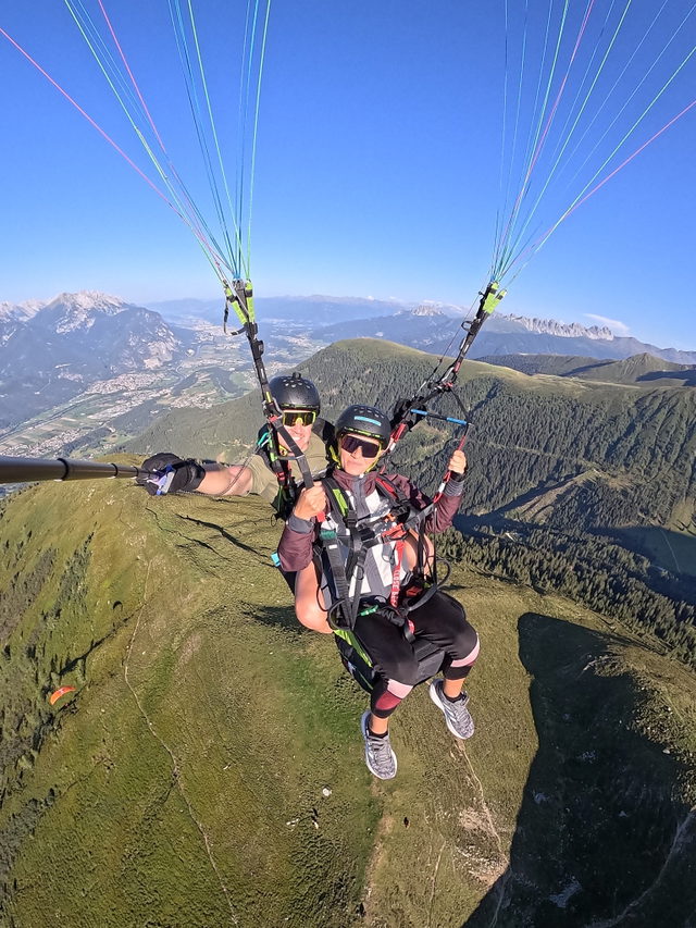 Zwei Personen beim Tandem-Paragleiten über grünen Bergrücken und Alpenpanorama