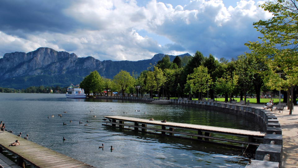 Seepromenade und Baumreihe am Mondsee mit Bergkulisse