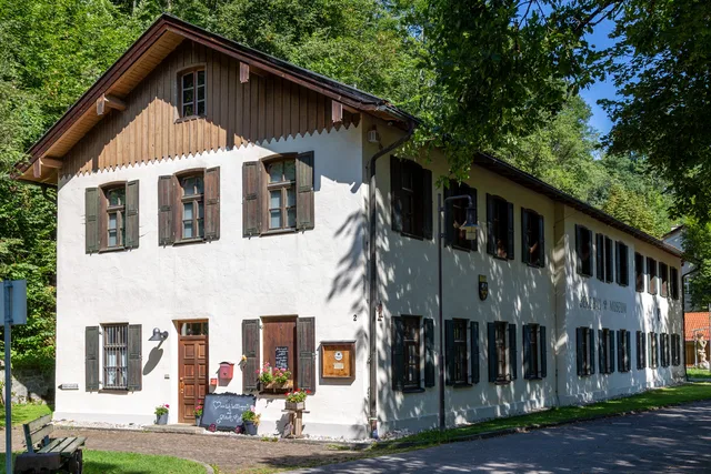 Weißes Haus mit braunen Fensterläden vor grüner Umgebung