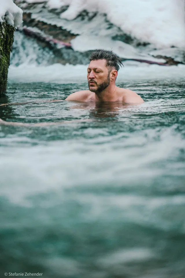 Mann beim Eisbaden in einem winterlichen Bach