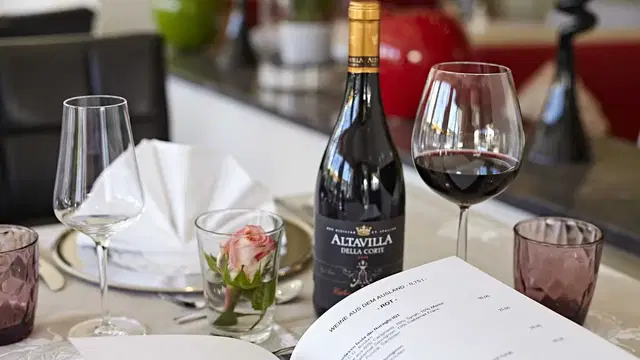 Weinflasche, Rotwein, Gläser und Menüblatt auf gedecktem Tisch