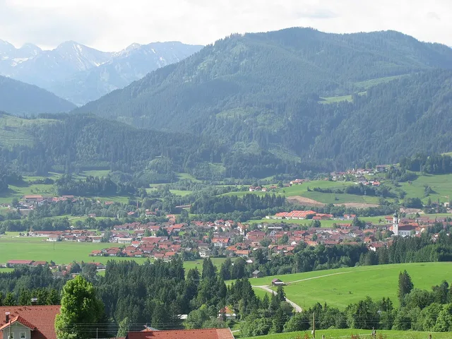 Landschaftsaufnahme des Oberallgäus: Tal, Dorf und grüne Wiesen vor bergigem Hintergrund.