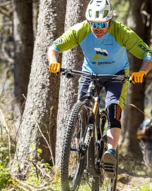 Mountainbiker im Wald mit Helm, Handschuhen und blau-grüner Jersey