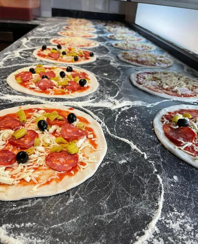 Mehrere Pizzen mit Tomatensauce, Käse, Pepperoni, Oliven und Paprika auf einer Thekenplatte.