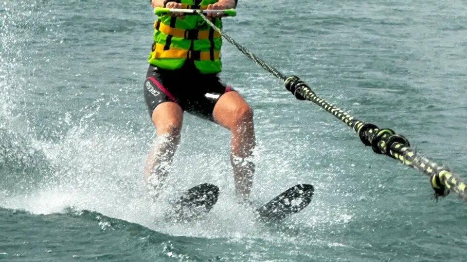 Wasserskifahrer mit Neon-Weste und Helm zieht an Bootleine über Wasser.