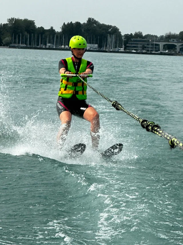 Wasserskifahrer mit Neon-Weste und Helm zieht an Bootleine über Wasser.