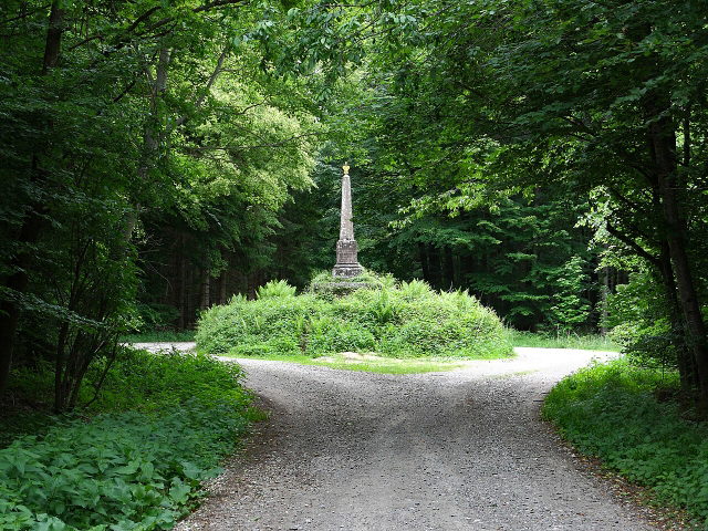 Behringer Denkmal an einer schattigen Weggabelung im Wald bei Boos