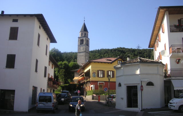Steinerner Turm der alten Pieve Santa Maria Assunta zwischen den Häusern von Baselga di Piné