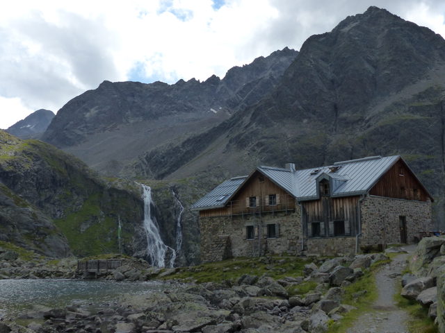 Winnebachseehütte mit Bergsee und Wasserfall vor alpiner Felskulisse