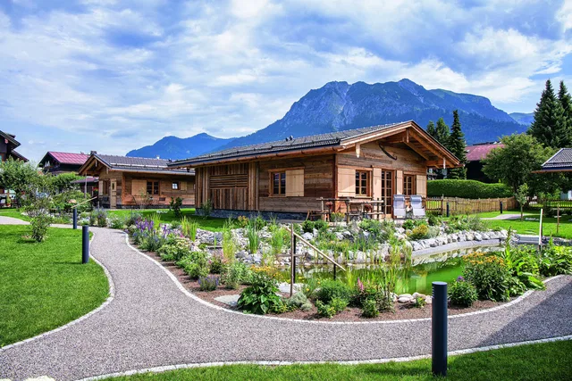Holz-Chalet in Alpenlandschaft mit Garten und Weg, Bergpanorama im Hintergrund.