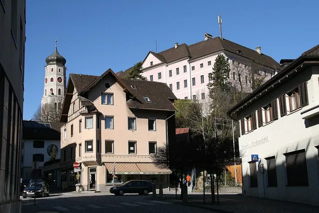 Straßenszene in Bludenz mit historischen Gebäuden und Kirchturm im Hintergrund.