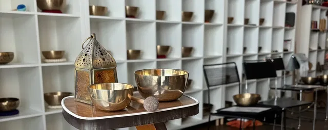Ausstellungsraum mit goldenen Schalen auf runden Tisch, Regale voller Schüsseln im Hintergrund.